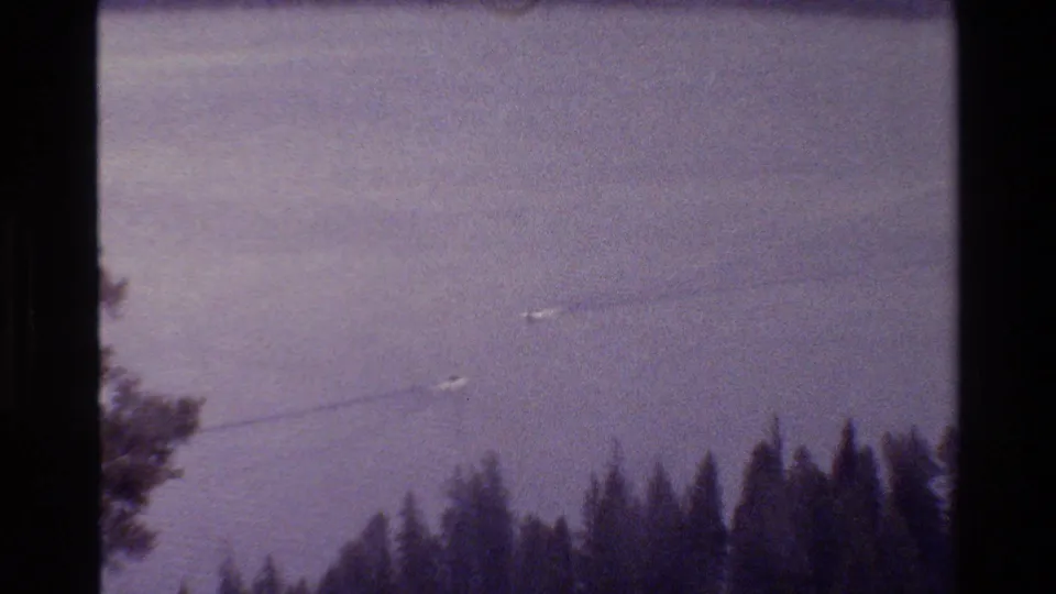 Grand Teton, Wyoming 1980 lake view with small boats and wakes above a dark evergreen shoreline in 8mm film framing.