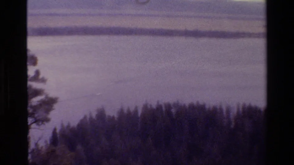 Grand Teton, Wyoming 1980 home-movie frame looking over a lake toward a distant shore, with evergreens low in frame.