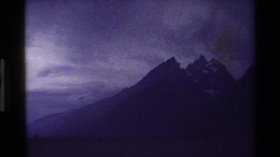 Grand Teton mountain peaks appear in silhouette beneath a cloudy, purple-shifted sky in 1980 8mm footage.
