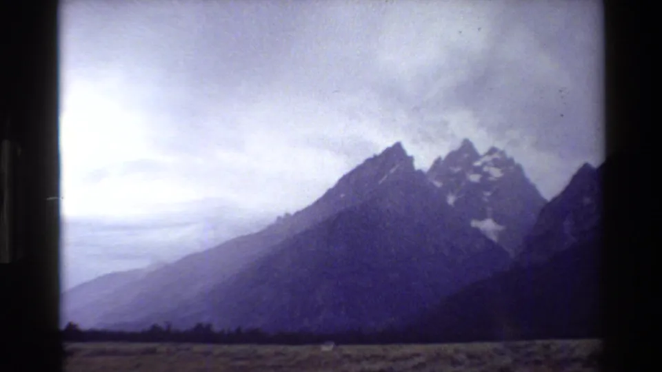 Grand Teton peaks and open valley are seen from a visitor viewpoint in soft, grainy 1980 8mm footage.