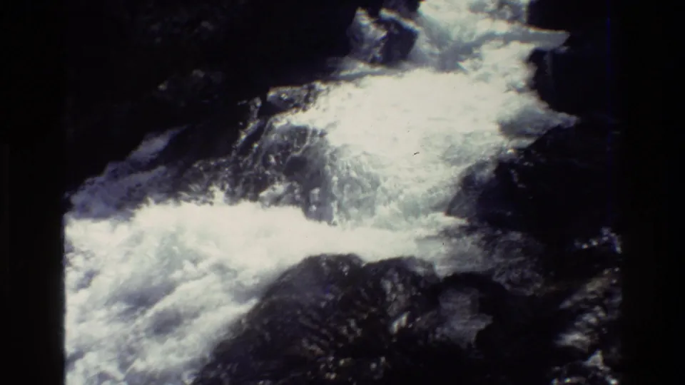1980 8mm Grand Teton-area footage showing frothy mountain water cascading over dark rocks in a shaded forest setting.