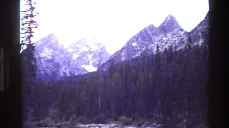1980 Grand Teton 8mm frame showing rugged mountain peaks above a dense evergreen forest under bright sky.