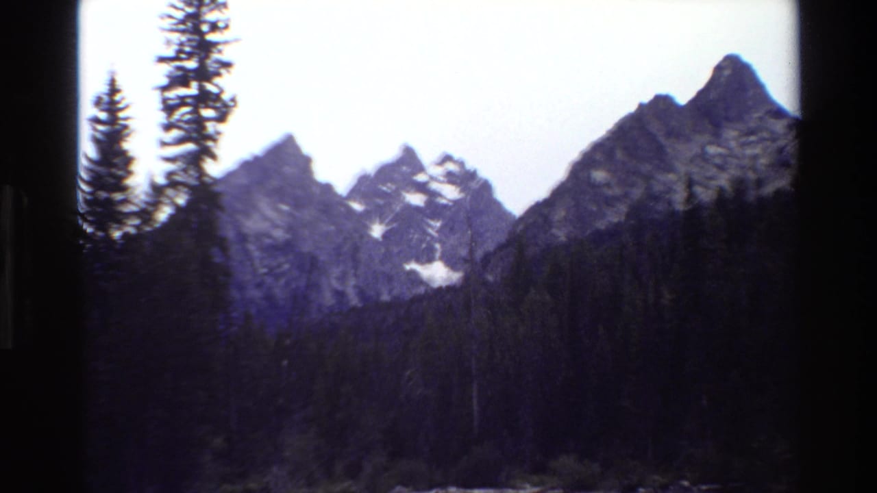 Grand Teton mountain range seen in faded 8mm color, with evergreen trees and dark frame borders around the view.