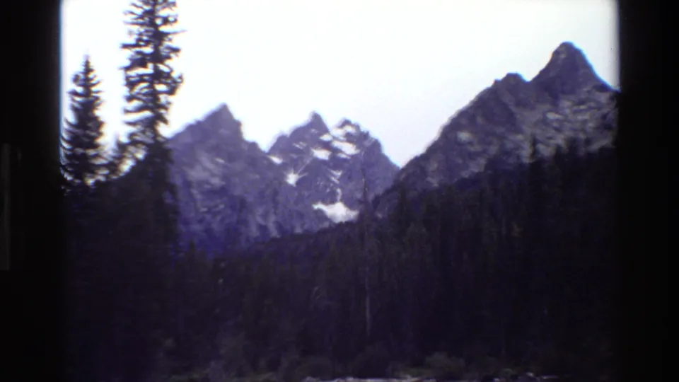 Grand Teton mountain range seen in faded 8mm color, with evergreen trees and dark frame borders around the view.