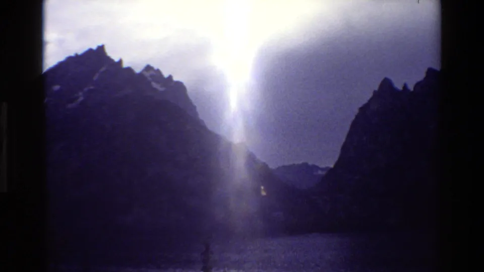 Grand Teton landscape frame with a bright white light flare over dark mountain silhouettes and a cool, faded 8mm look.