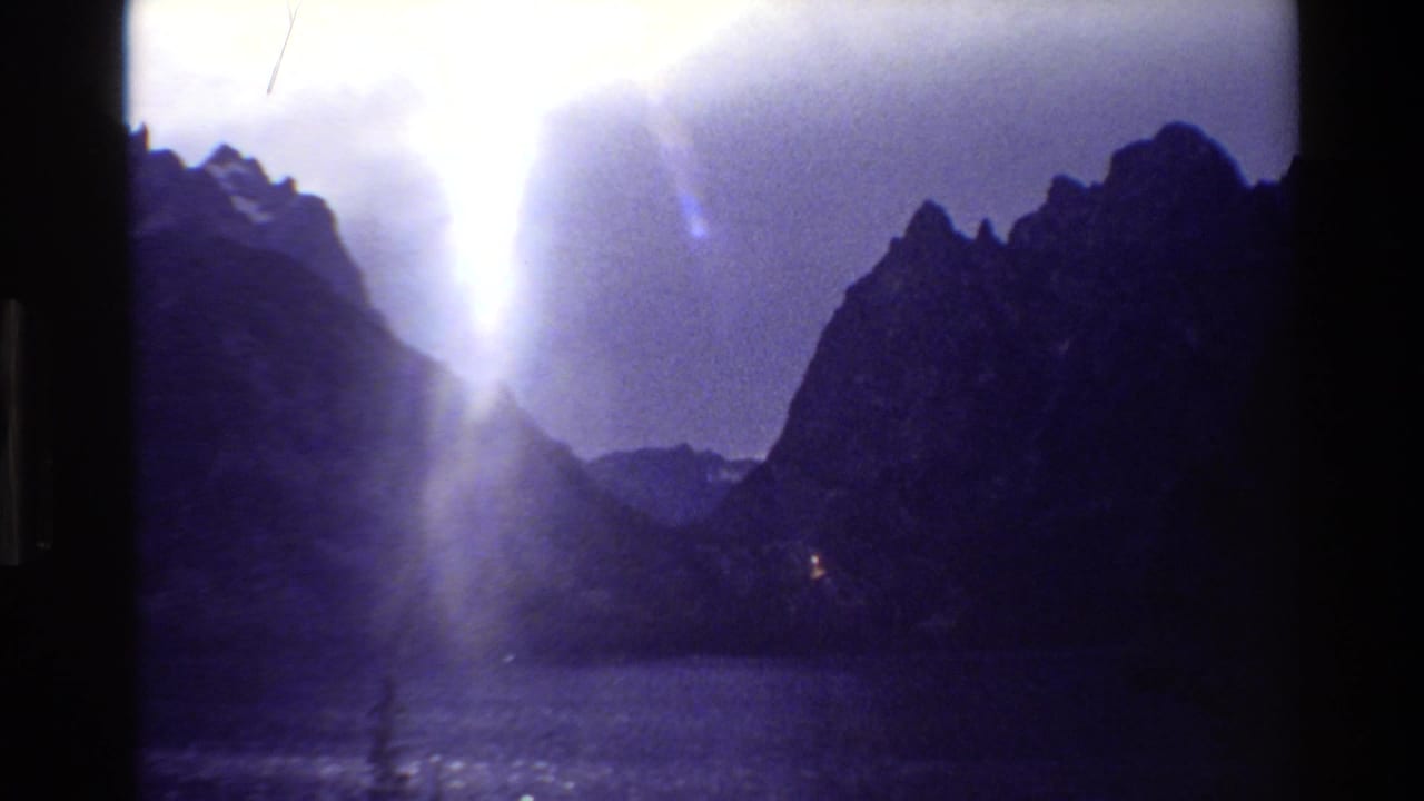 Mountain lake and rugged peaks under clouds with a bright vertical beam of sunlight.