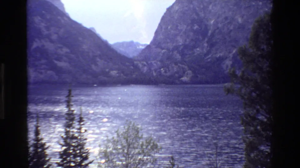 Grand Teton 8mm lakeside view with sparkling water, foreground trees, and steep rocky mountains in soft vintage color.