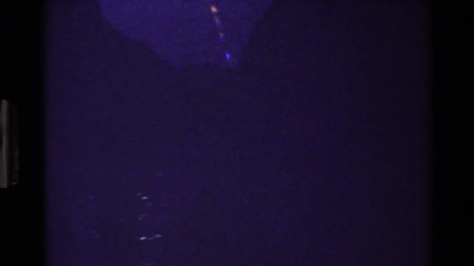 Low-light 8mm frame with heavy purple color cast and faint, indistinct outdoor landscape detail.