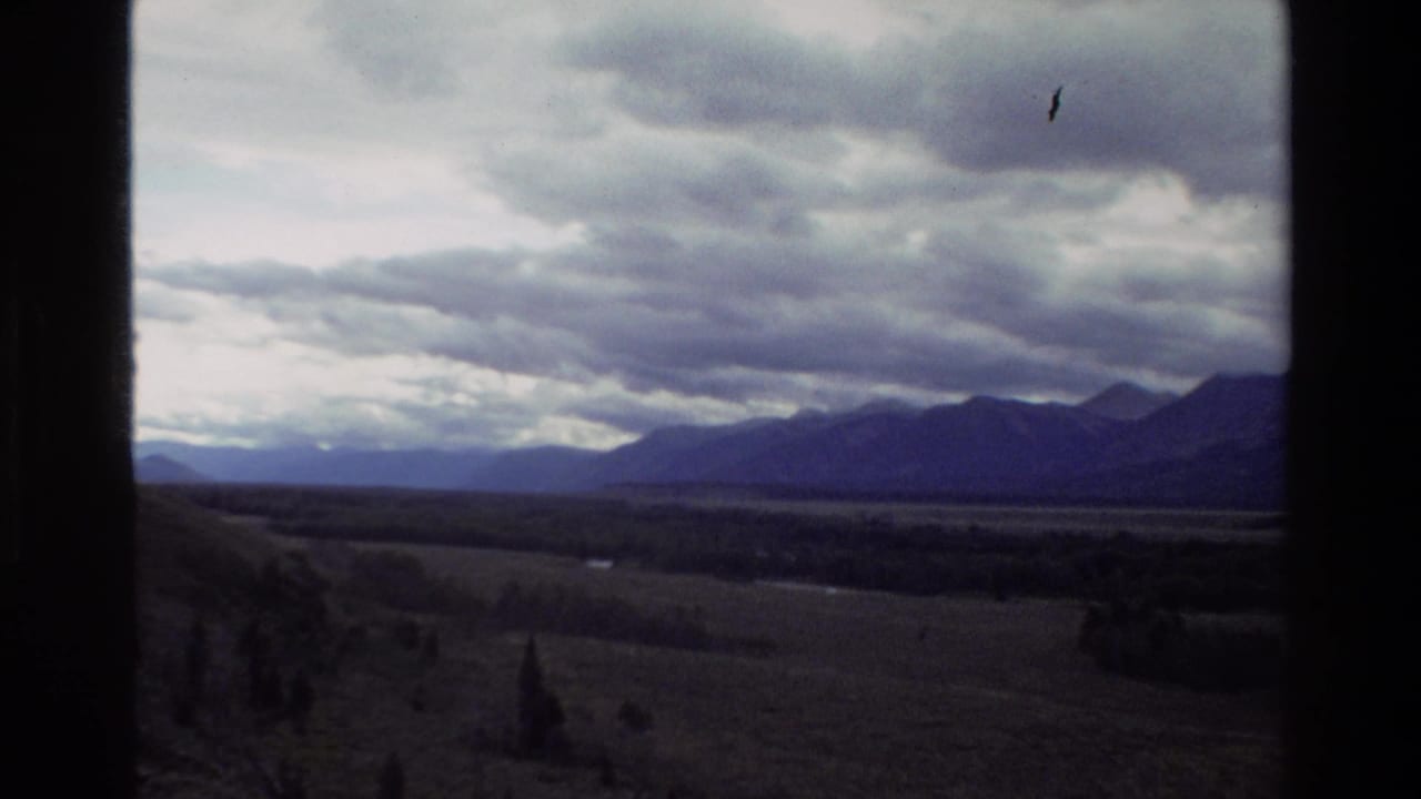 Wide valley and mountain ridge under heavy clouds, bordered by dark window framing.