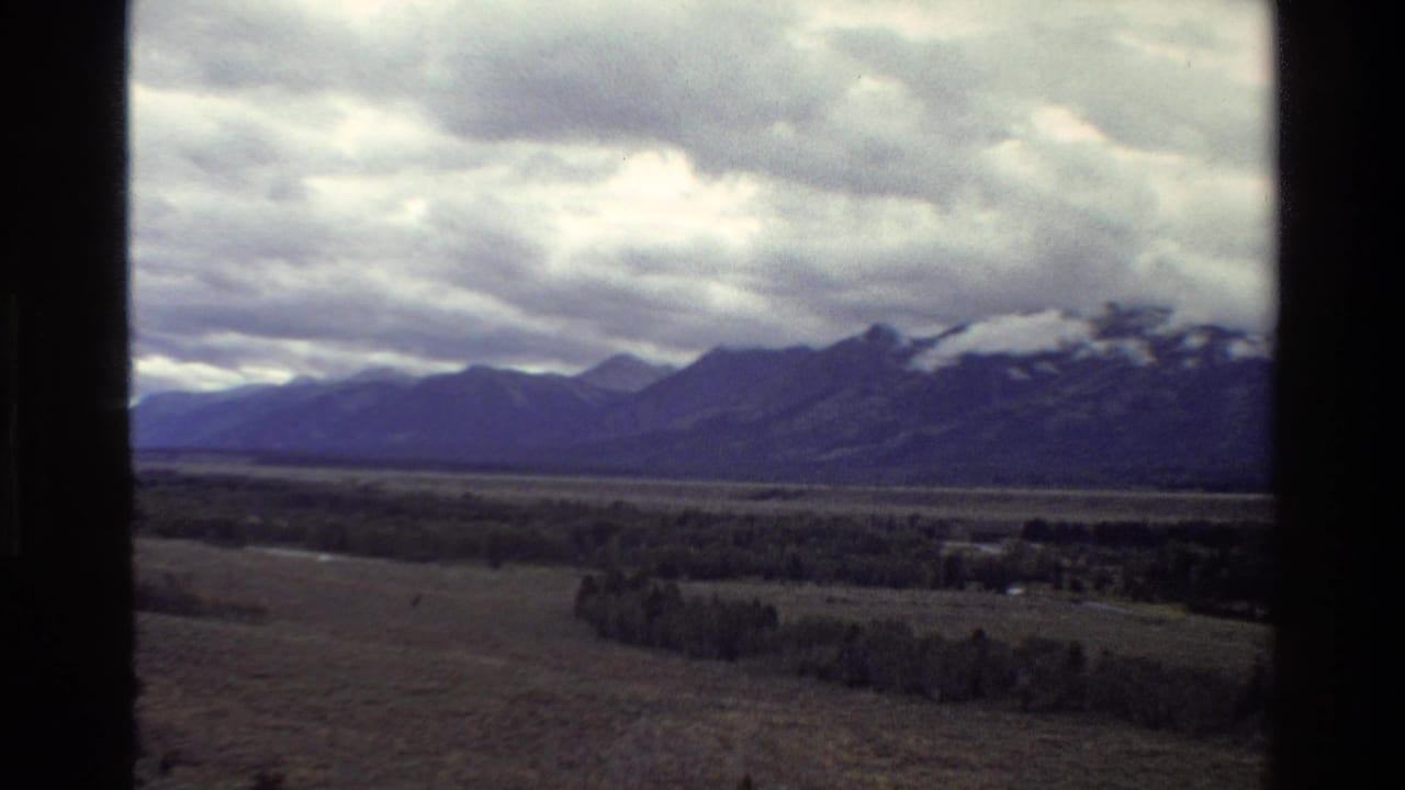 Distant mountains and valley fields under dense clouds, partially bordered by dark vertical edges.