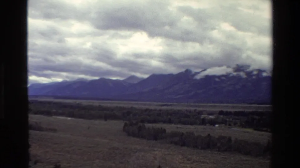 Grand Teton, Wyoming landscape from 1980 home-movie footage, showing mountains, valley floor, trees, and a cloudy sky.