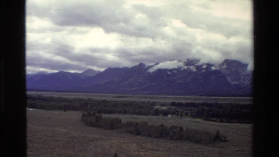 1980 8mm frame of the Grand Teton range with low clouds over the peaks and open Wyoming valley below.