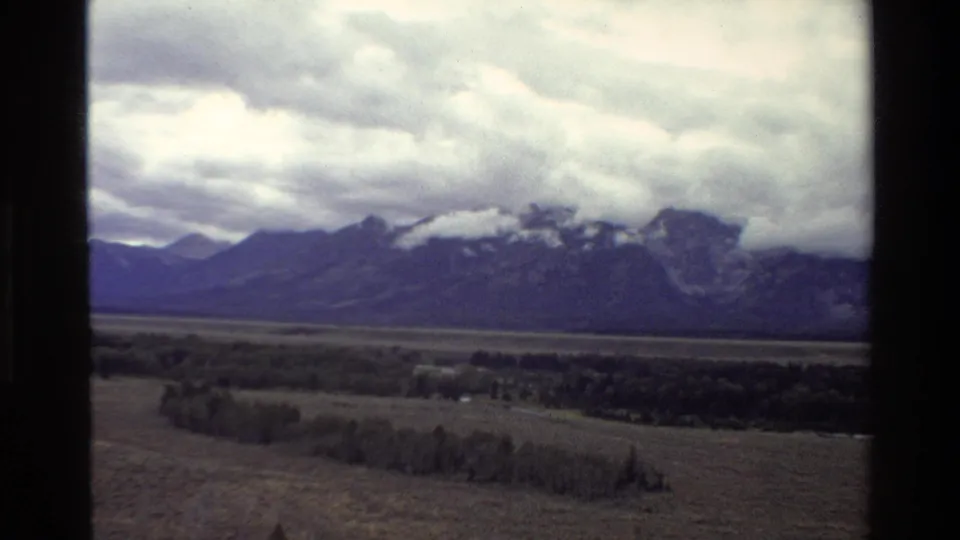 End of a 1980 Grand Teton 8mm pan showing a clouded mountain ridge, valley vegetation, and dark home-movie frame borders.