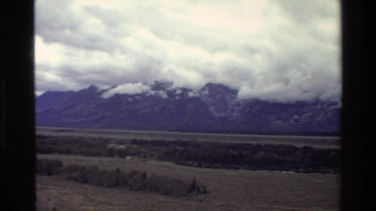 Mountain ridge and broad valley beneath a cloudy sky, framed by 8mm film edges.