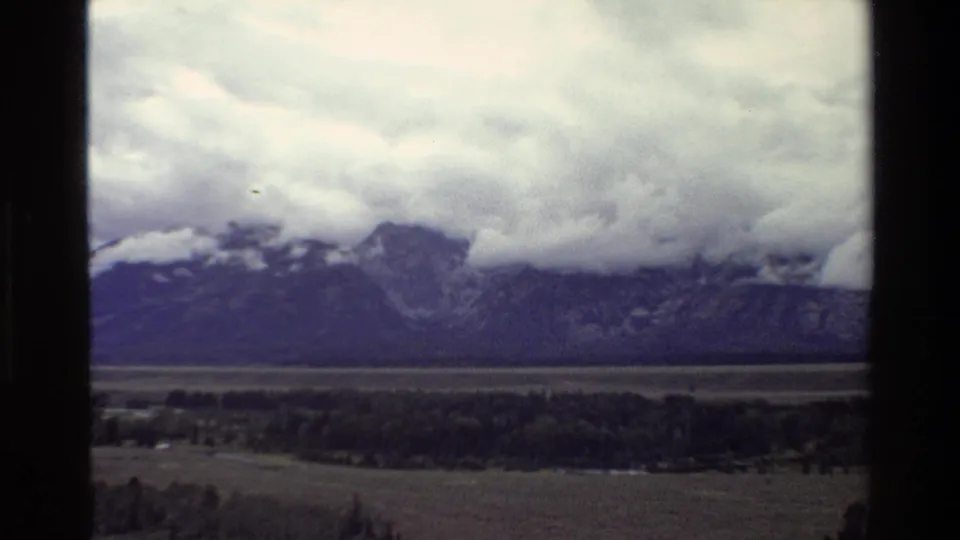 Final 8mm frame of the Grand Teton landscape, showing dark mountains, heavy cloud cover, a valley floor, and scattered trees.