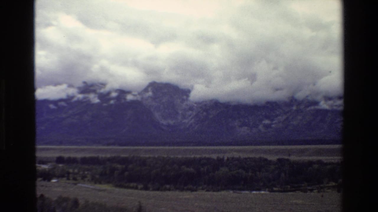 1980 8mm view of storm clouds over the Grand Teton mountain range and valley, partly framed by a dark window edge.