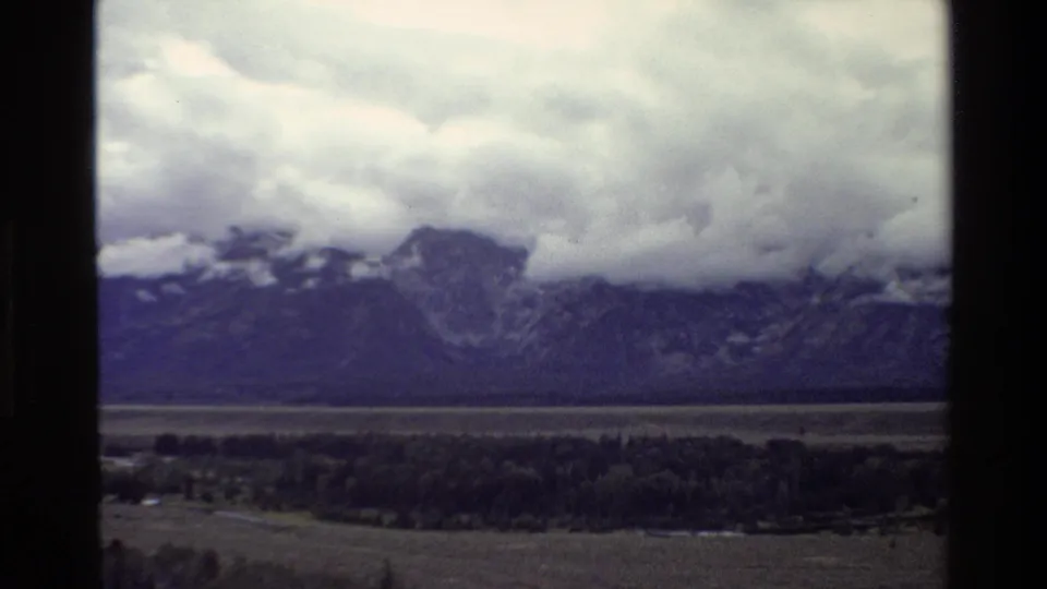 1980 8mm view of storm clouds over the Grand Teton mountain range and valley, partly framed by a dark window edge.