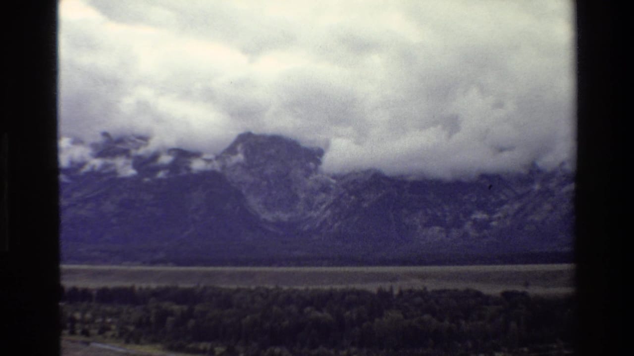 Mountain peaks under heavy clouds with a valley and trees below.