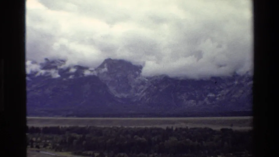 Grand Teton, Wyoming landscape in 1980 8mm footage, with low storm clouds over peaks and a wooded valley below.