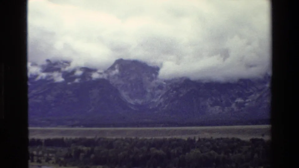 End frame of 1980 Grand Teton 8mm footage showing a cloud bank over dark peaks, with valley trees below.