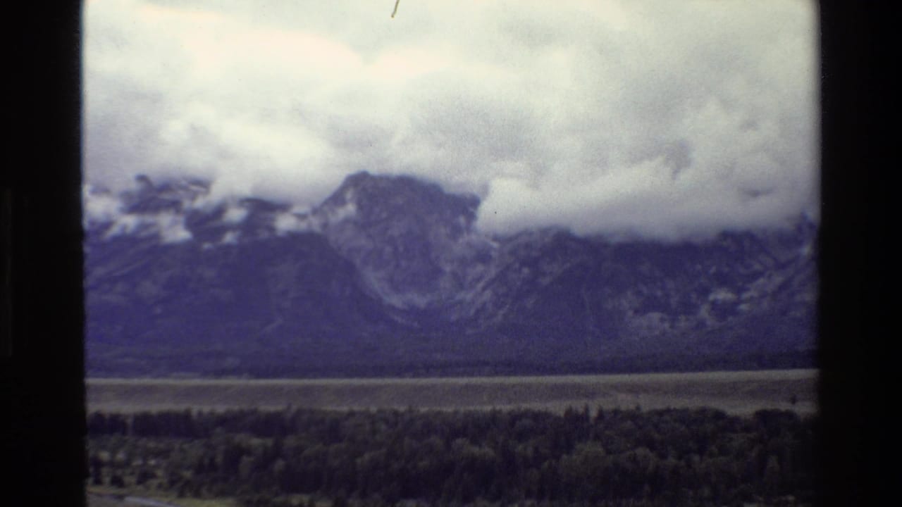 Mountain range under low clouds above a forested valley.