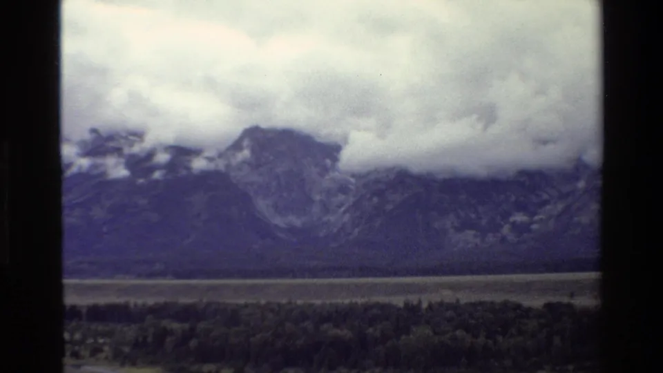 Grand Teton, Wyoming landscape frame with dark forest in front of a mountain range partially hidden by moving cloud cover.