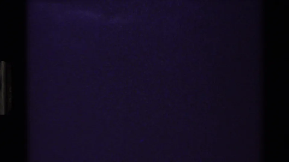 Underexposed 8mm frame from the Grand Teton clip, showing blue-purple film texture with gate edges and minimal landscape detail.