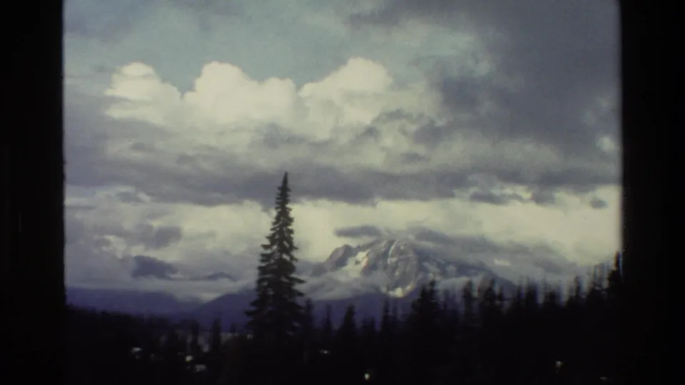 1980 Grand Teton, Wyoming 8mm still showing a snowy mountain partly veiled by clouds, with dark evergreens in the foreground.