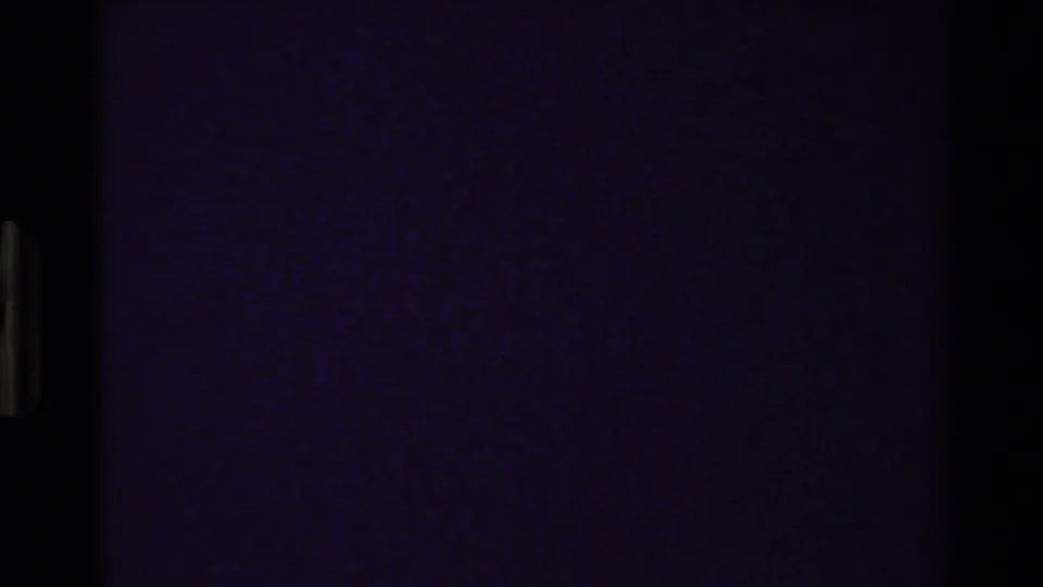 A mostly dark, purple-tinted 8mm frame from the Grand Teton sequence, likely a transition or underexposed moment with minimal visible detail.