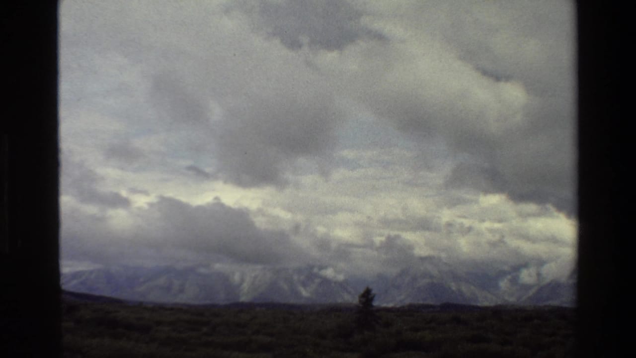 1980 Grand Teton 8mm frame showing heavy clouds above distant mountains and dark foreground scrubland.