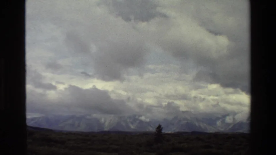 1980 Grand Teton 8mm frame showing heavy clouds above distant mountains and dark foreground scrubland.
