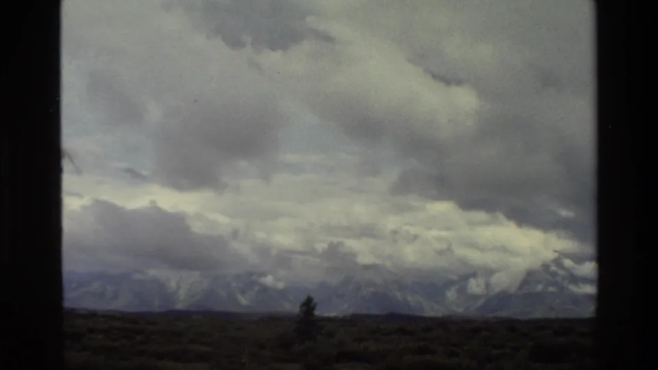 1980 Grand Teton 8mm frame with thick gray clouds crossing the mountain skyline above open land.