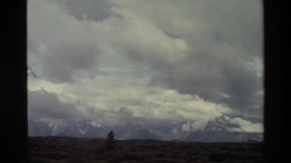 1980 Grand Teton 8mm frame showing a wide stormy sky over mountains, scrubland, and a lone evergreen.