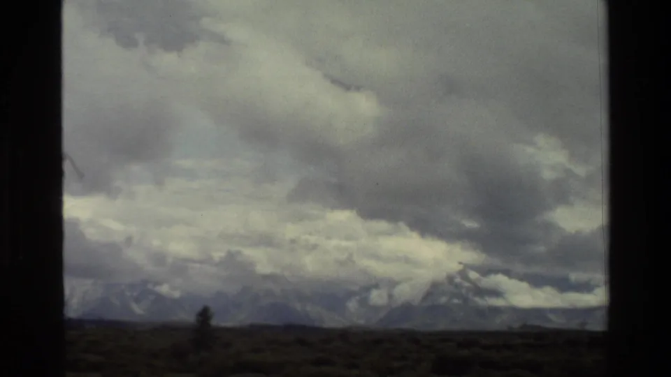 1980 Grand Teton 8mm frame with pale and dark clouds over distant peaks and sparse foreground vegetation.