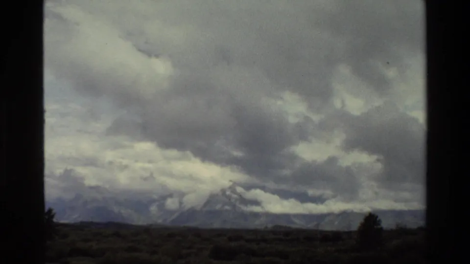 Grand Teton, Wyoming landscape in 1980 8mm footage, showing heavy clouds above snow-streaked peaks and a dark open foreground.
