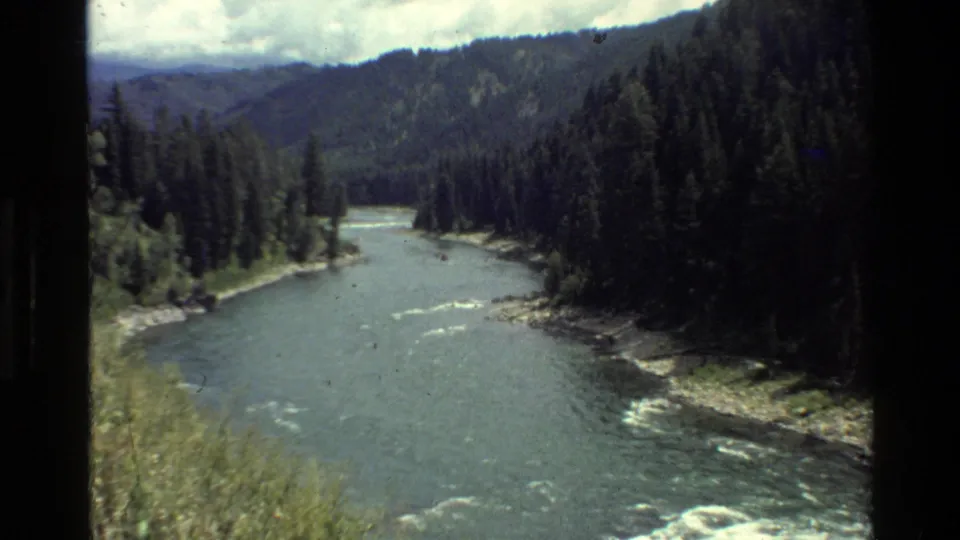 Wide 1980 Grand Teton, Wyoming view of a river running through evergreen forest and mountain slopes.