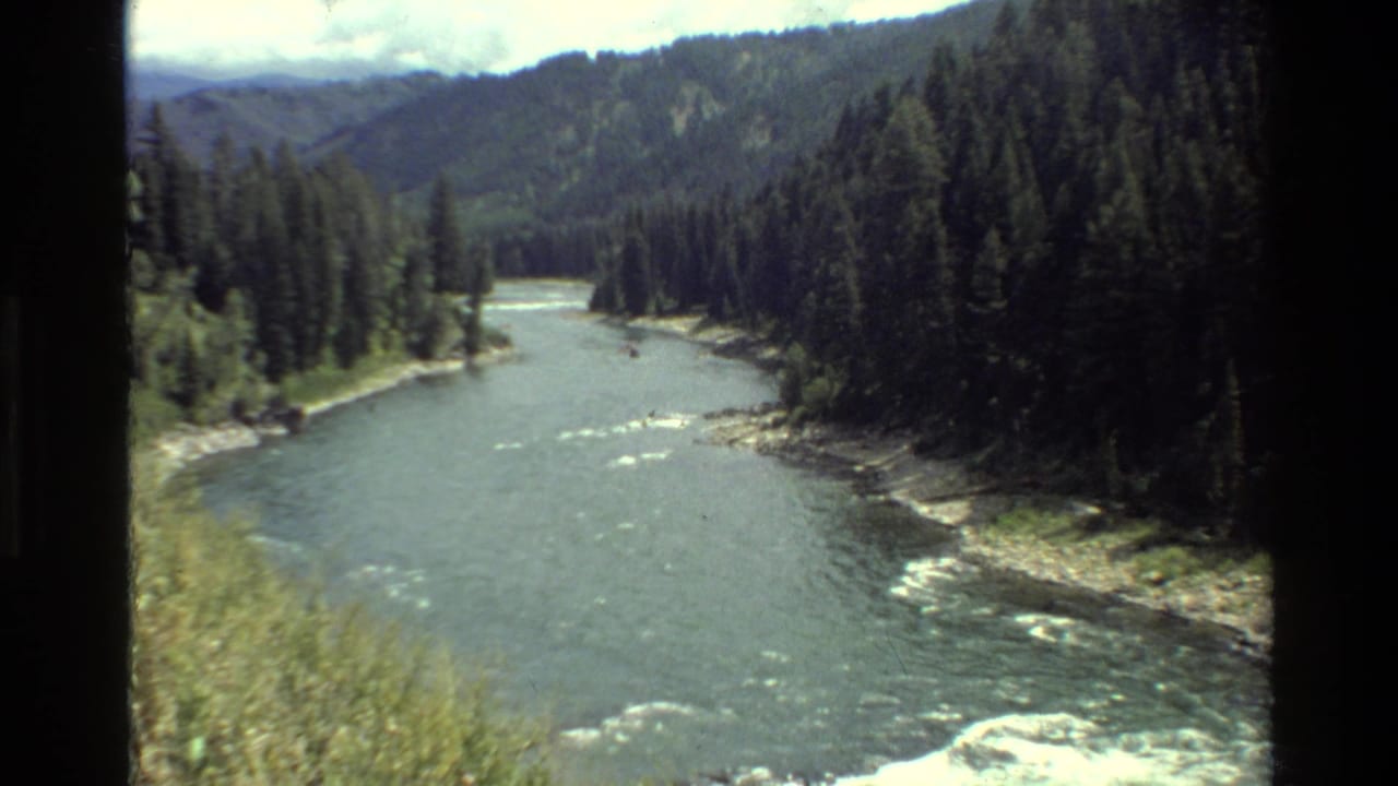 1980 Grand Teton 8mm view of a winding river below evergreen slopes, with mountains and cloud cover in the distance.
