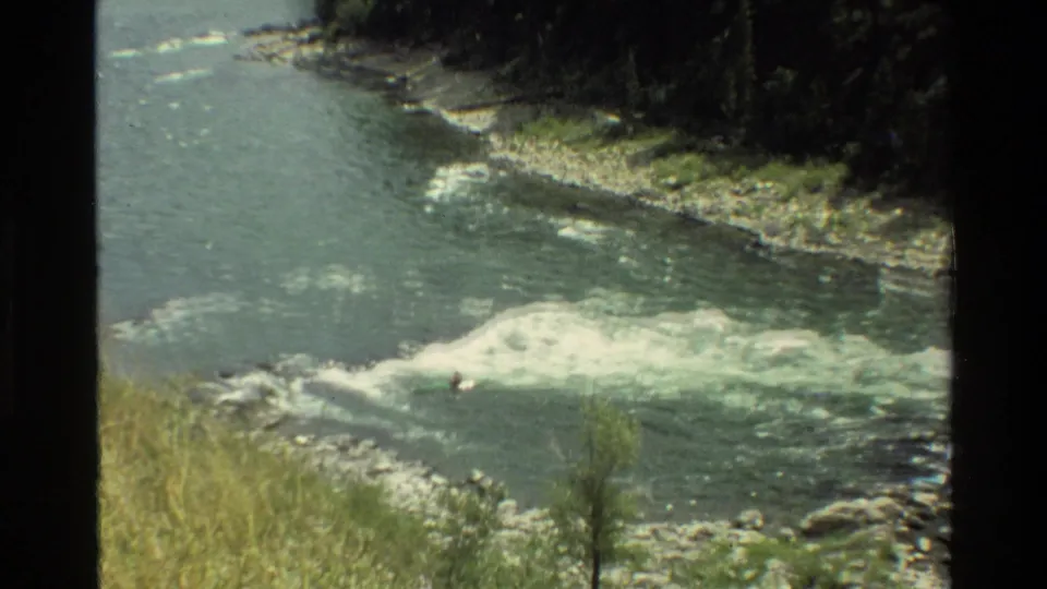 Closer 8mm view of rapids in a Wyoming river, with a distant kayaker entering the white water near the foreground.