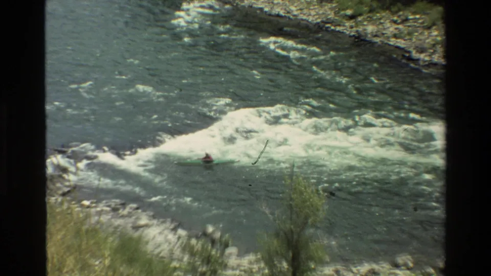 Distant person in a green kayak navigates white-water rapids on the Grand Teton river, filmed from above on 8mm.