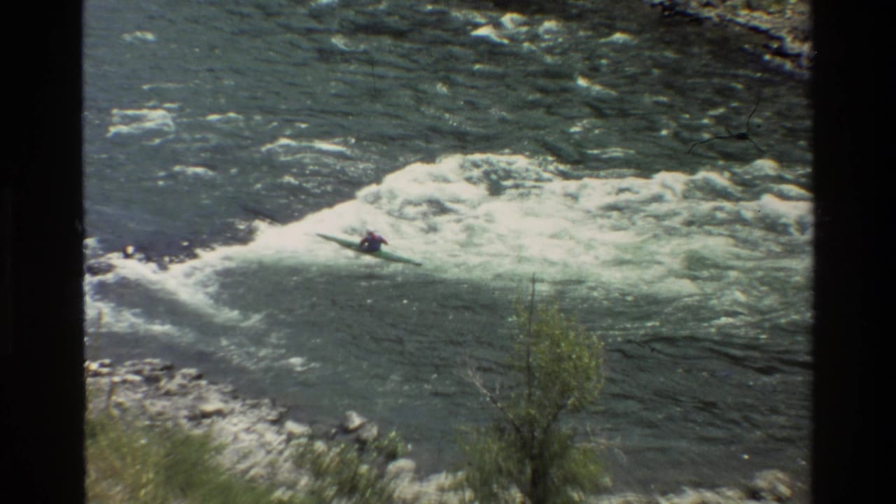 Kayaker paddles across foaming rapids near the center of the river.