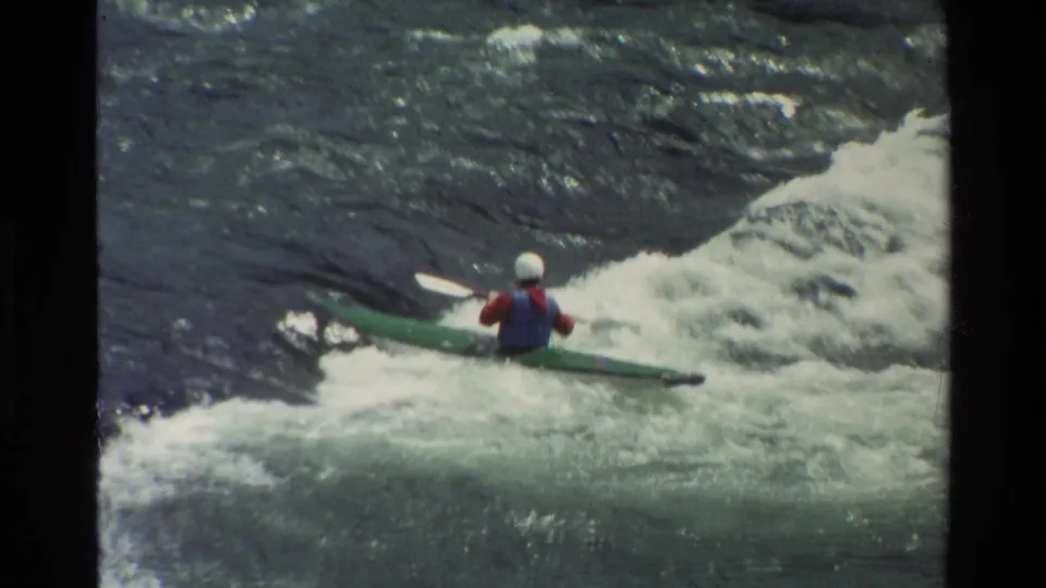 Rear-facing 1980 Grand Teton, Wyoming home-movie frame of a paddler in safety gear moving through rapids.