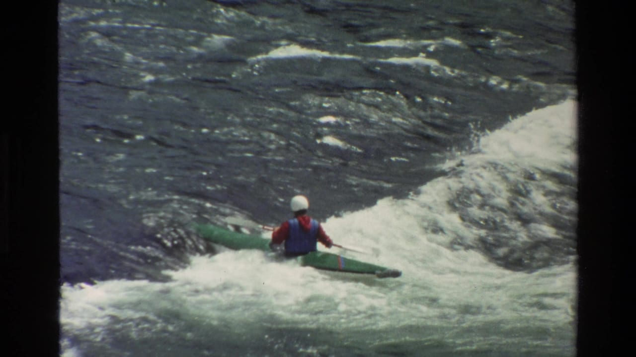1980 Grand Teton, Wyoming home-movie frame showing a helmeted kayaker in a green kayak amid foaming rapids.