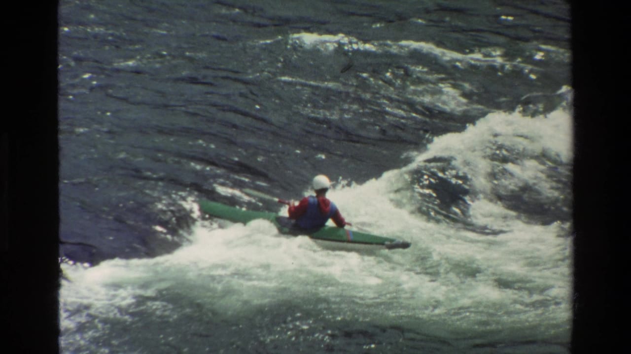 Kayaker riding over a wave in whitewater rapids.