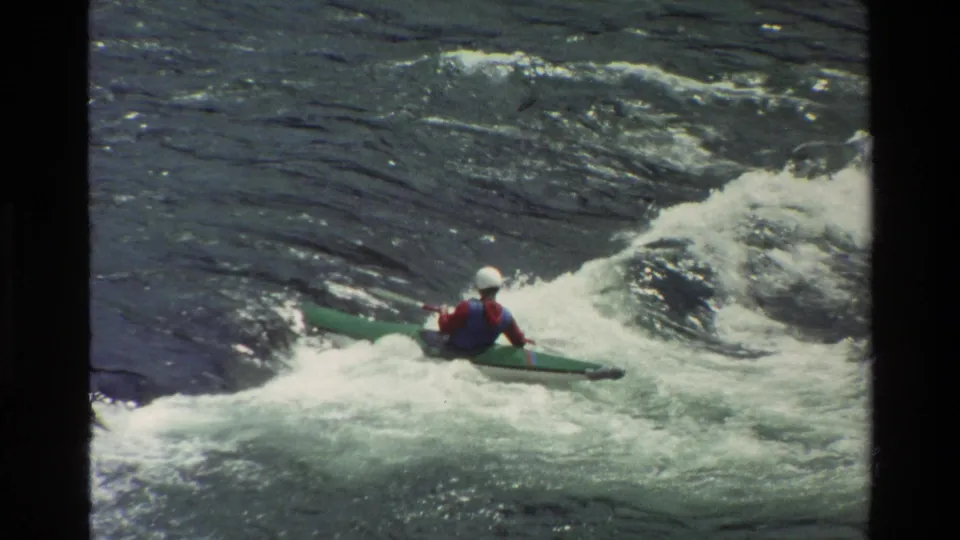 Helmeted kayaker in a green boat rides through foamy rapids in the Grand Teton, Wyoming footage.