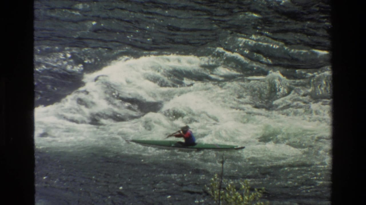 A helmeted kayaker in a green kayak moves through churning rapids in Grand Teton, Wyoming, in 1980 8mm footage.