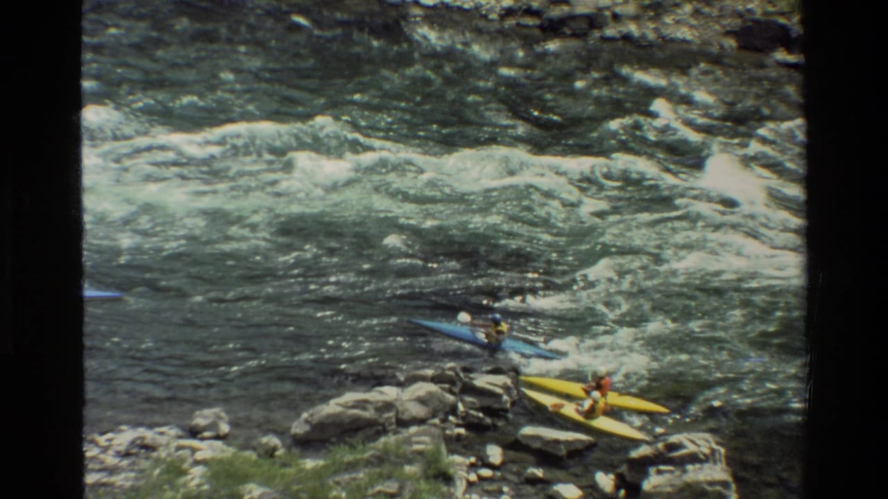 Blue and yellow kayaks near rocks beside fast-moving river water.
