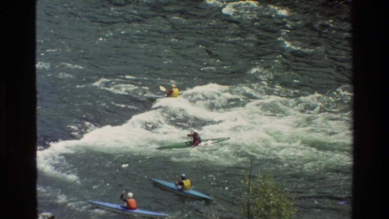 1980 home-movie frame from Grand Teton, Wyoming, showing kayakers in bright vests moving through whitewater rapids.