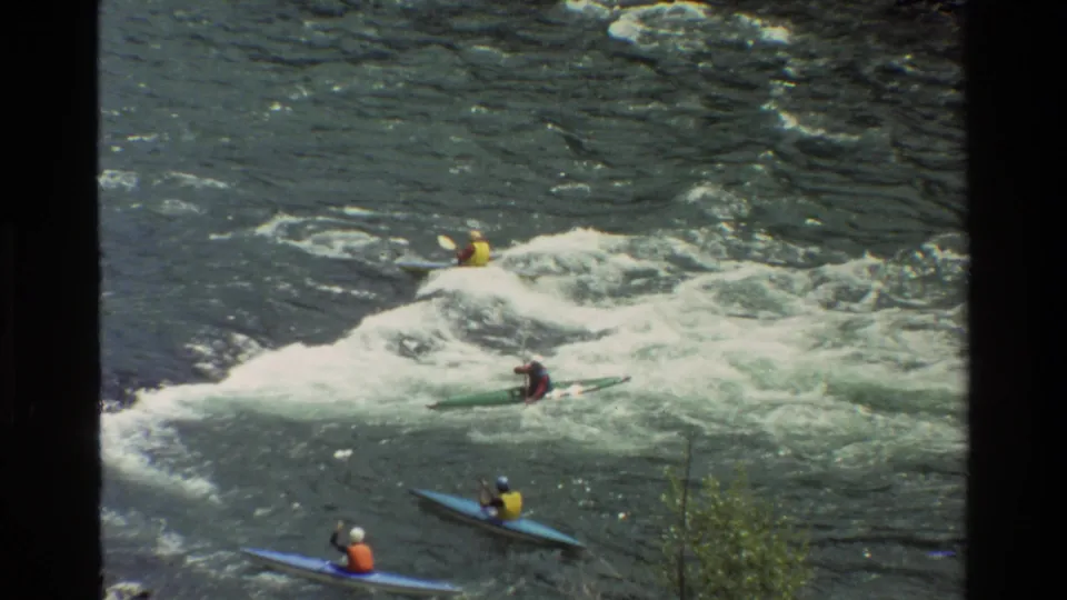1980 home-movie frame from Grand Teton, Wyoming, showing kayakers in bright vests moving through whitewater rapids.