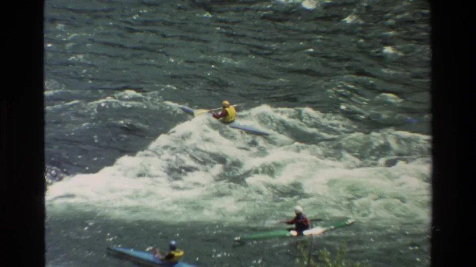 1980 8mm frame of kayakers in Grand Teton, Wyoming, moving through a broad whitewater wave on the river.