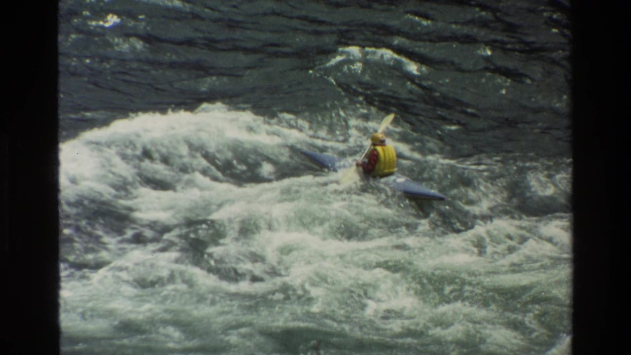 1980 Grand Teton home-movie frame showing a kayaker in a yellow life jacket navigating foamy whitewater.